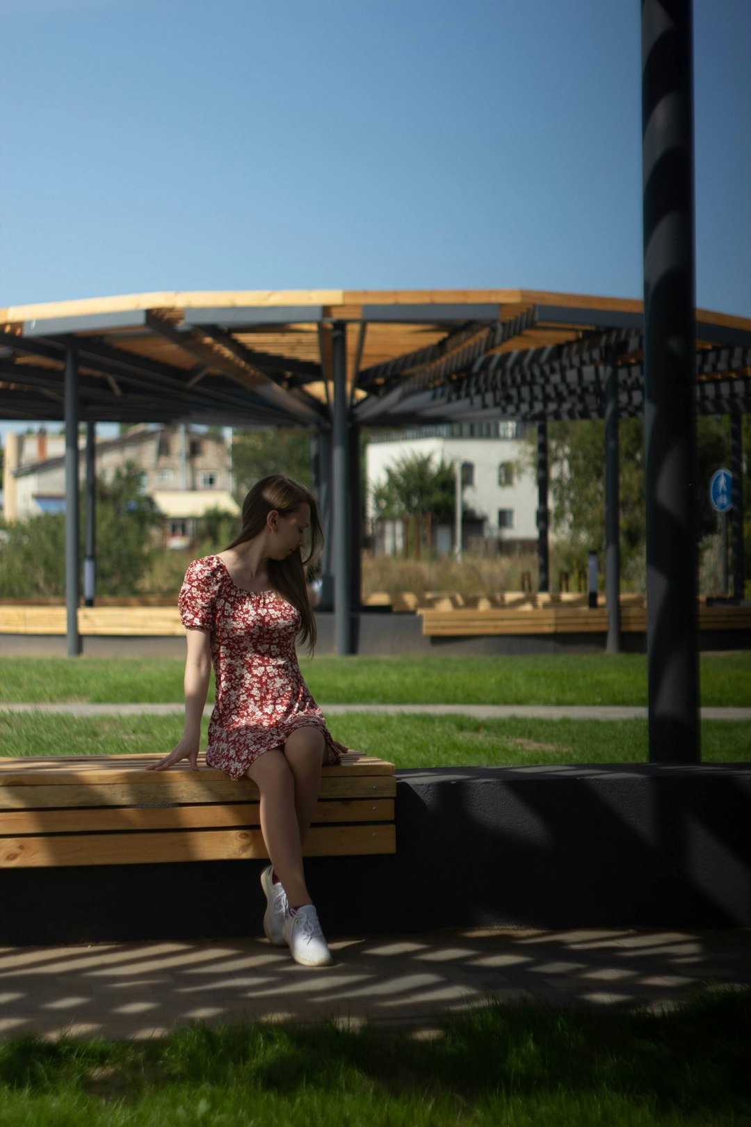 woman in pink and white floral dress sitting on brown wooden bench during daytime