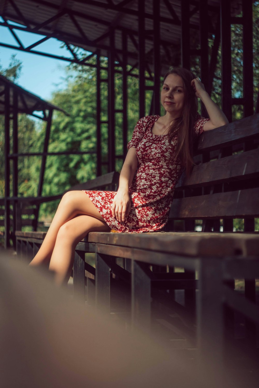 茶色の木製のベンチに座っている黒と赤の花柄のドレスを着た女性