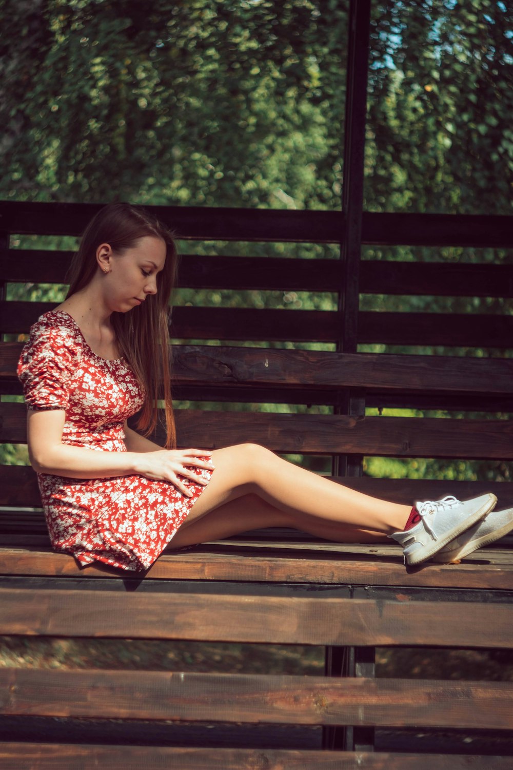 woman in black red and white floral dress sitting on brown wooden bench