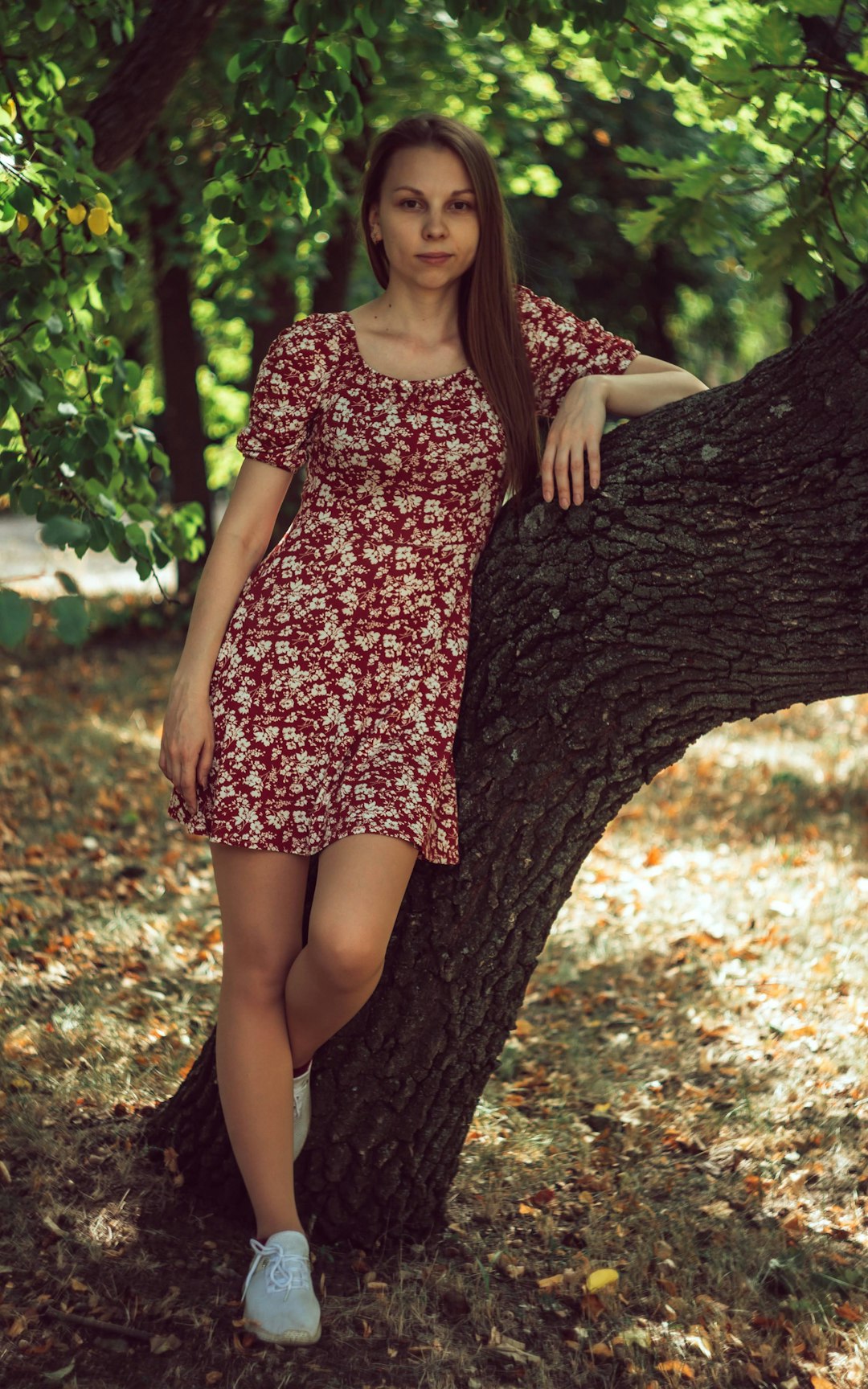 woman in red and white floral dress leaning on tree