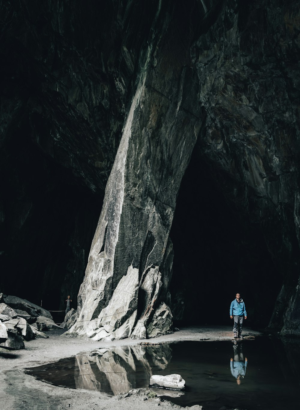 uomo in camicia blu e jeans blu denim in piedi sulla sabbia marrone vicino alla montagna rocciosa durante