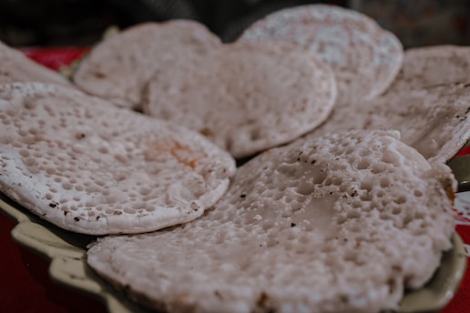 A close-up of a rustic wooden plate with freshly made pão de queijo, the famous Brazilian cheese bread, steaming and golden-brown.