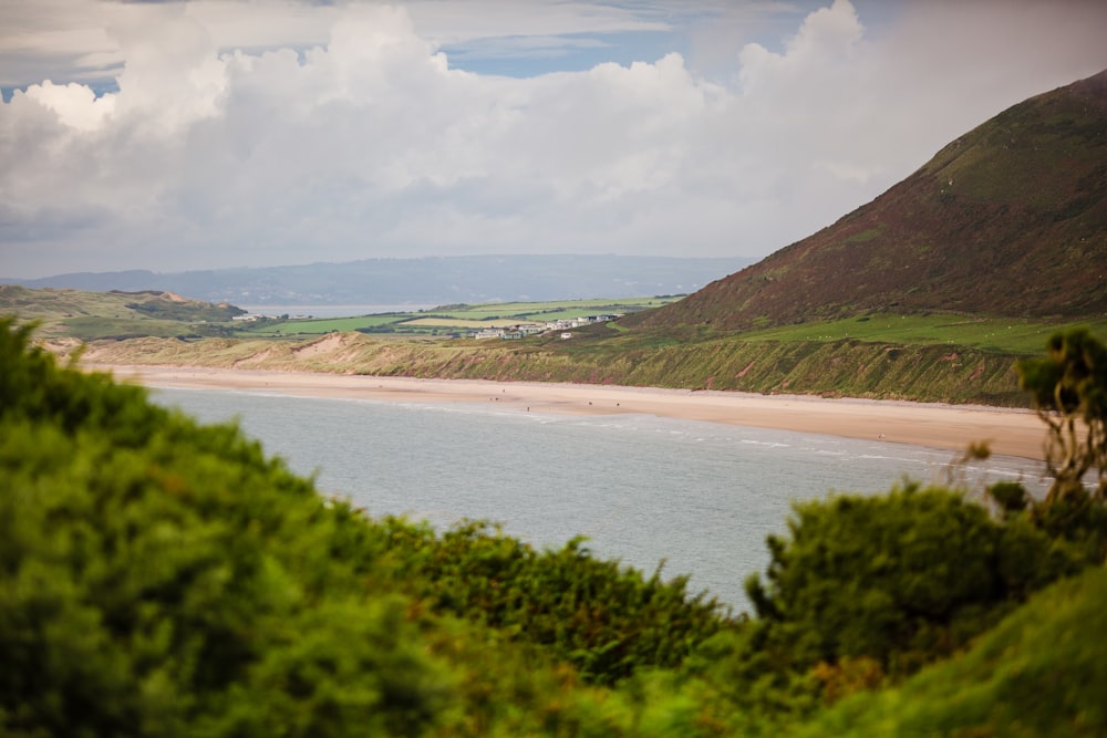 green mountain beside body of water under white clouds during daytime