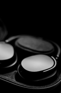 A pair of sleek, modern over-ear headphones placed inside an open, fabric-lined case. The lighting highlights the smooth, matte finish of the headphones against a dark background, creating a sense of luxury and sophistication.