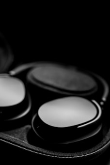 A pair of sleek, modern over-ear headphones placed inside an open, fabric-lined case. The lighting highlights the smooth, matte finish of the headphones against a dark background, creating a sense of luxury and sophistication.