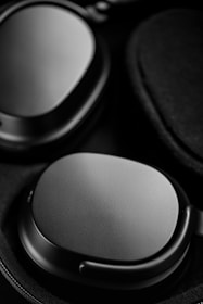 A close-up image of high-quality black over-ear headphones with a smooth, matte texture. The focus is on the ear cups, highlighting their sleek design and premium material.