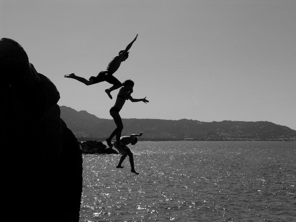 grayscale photo of 2 men jumping on water