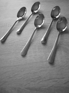 Close-up of shiny metal spoons and forks arranged neatly on a wooden table.