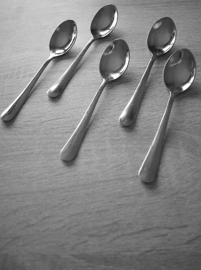 Close-up of shiny metal spoons and forks arranged neatly on a wooden table.