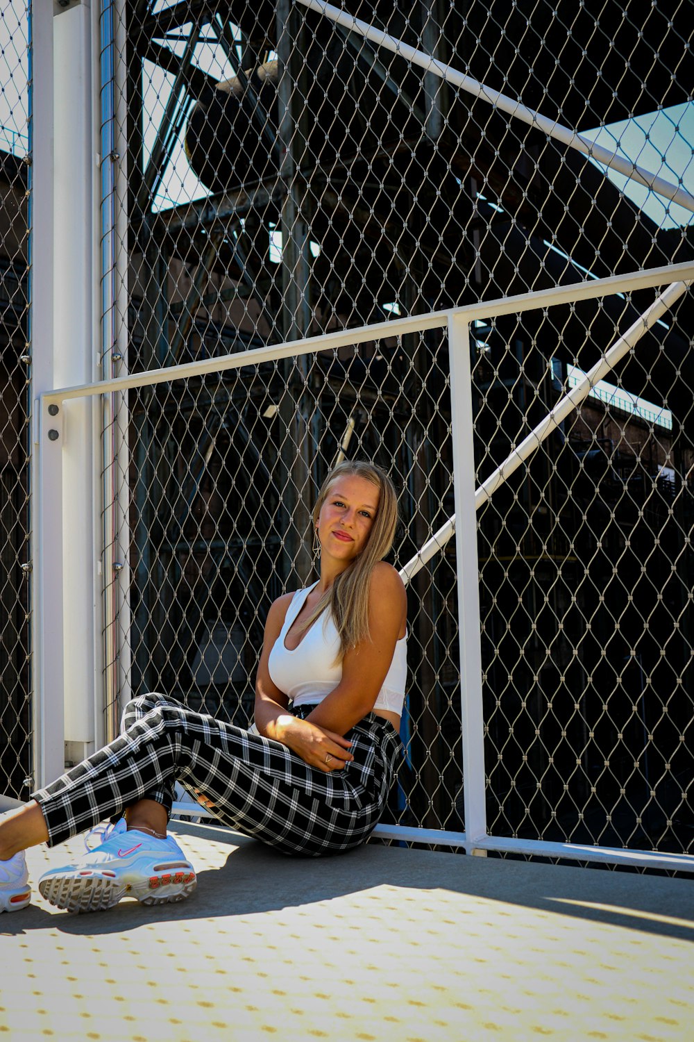 woman in white tank top and black and white pants sitting on white metal fence