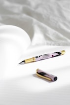 Elegant ballpoint pens embedded with pressed flowers arranged on a black and white fabric.