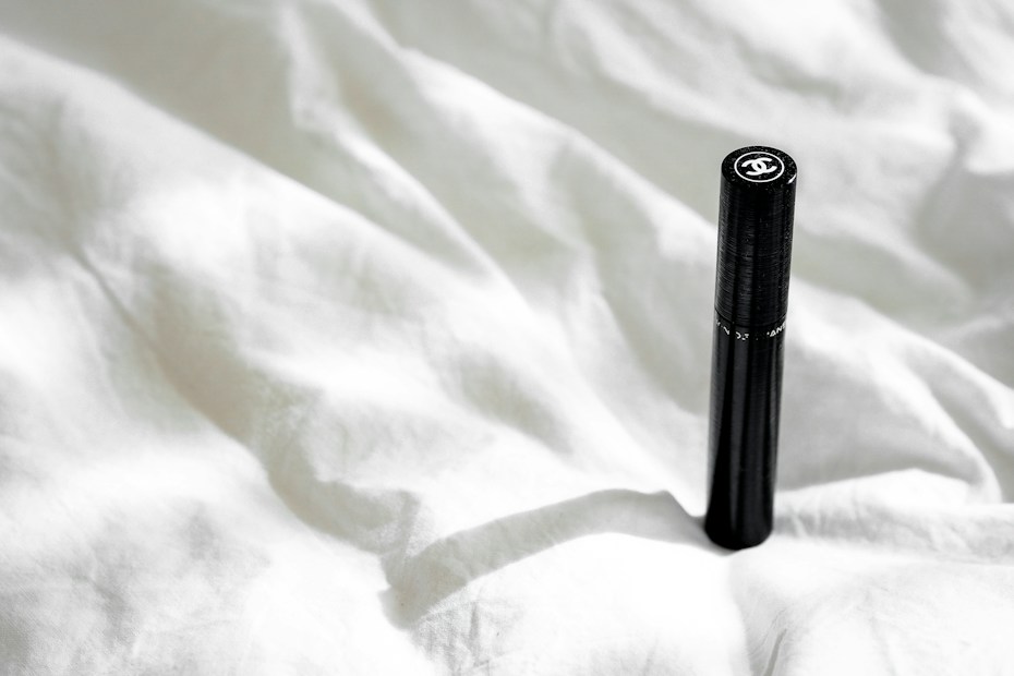 A sleek black cylindrical object with a logo on top is positioned upright on a crumpled white fabric surface. Natural light casts a soft shadow, adding subtle depth to the texture of the fabric.