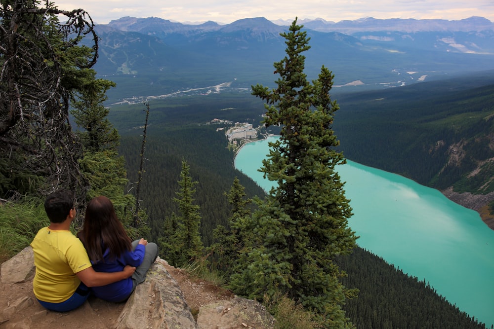 woman in blue shirt sitting on rock near lake during daytime