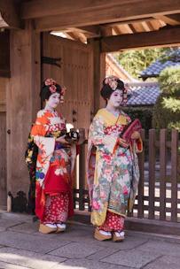 woman in white red and green floral kimono standing beside brown wooden fence during daytime