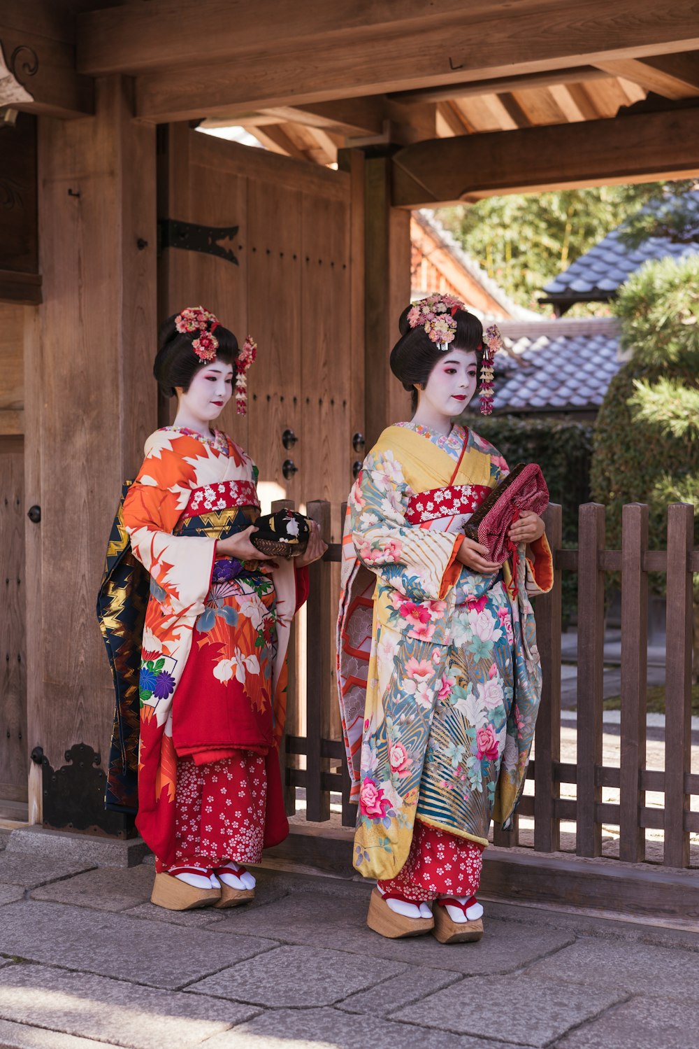 woman in white red and green floral kimono standing beside brown wooden fence during daytime