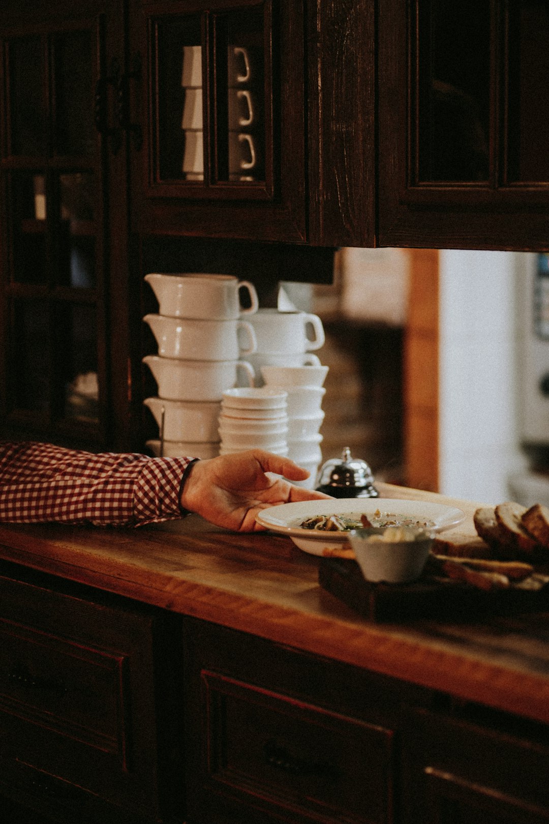 person in black and white checkered long sleeve shirt holding white ceramic teacup on brown wooden