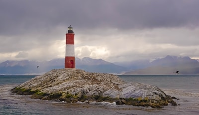 red and white lighthouse on brown rock formation near body of water during daytime