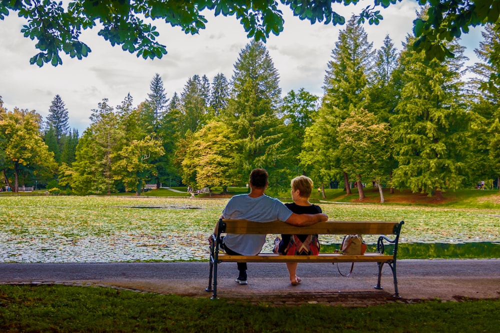 man and woman sitting on bench near lake during daytime
