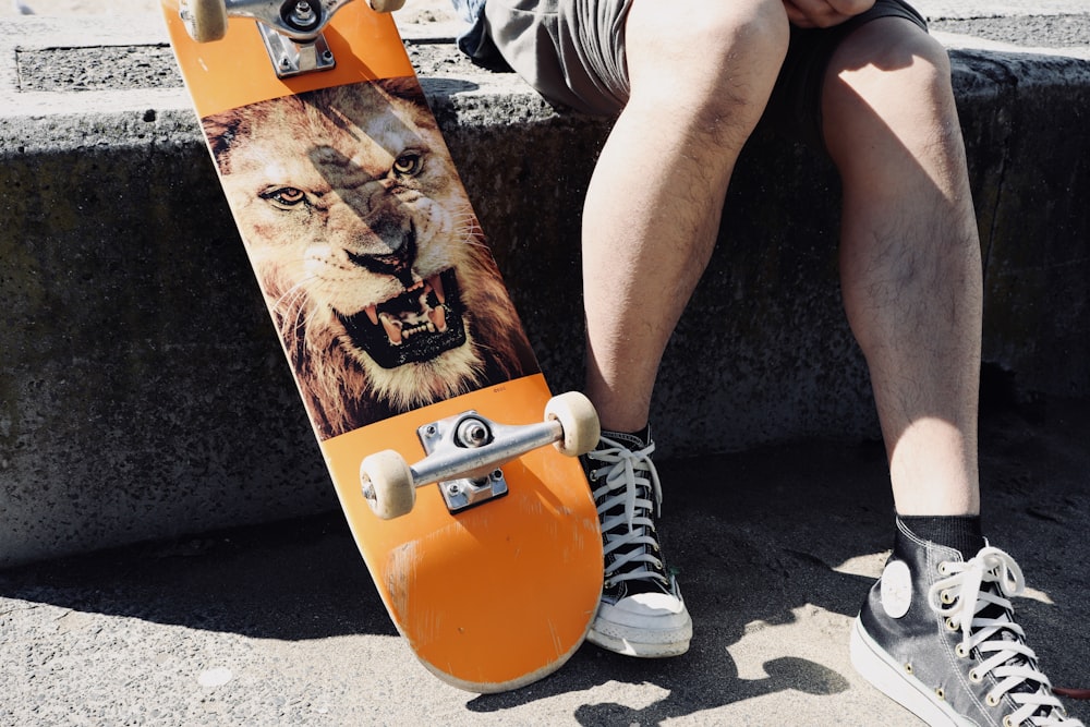 person in white and black stripe shorts sitting on orange skateboard during daytime