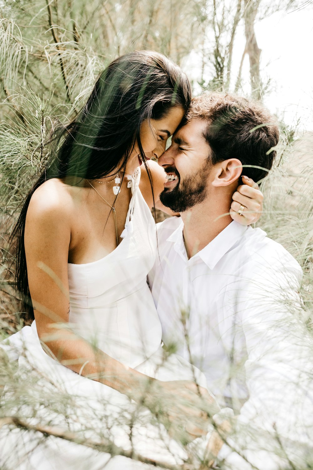 homem na camisa social branca beijando a mulher no vestido branco sem mangas