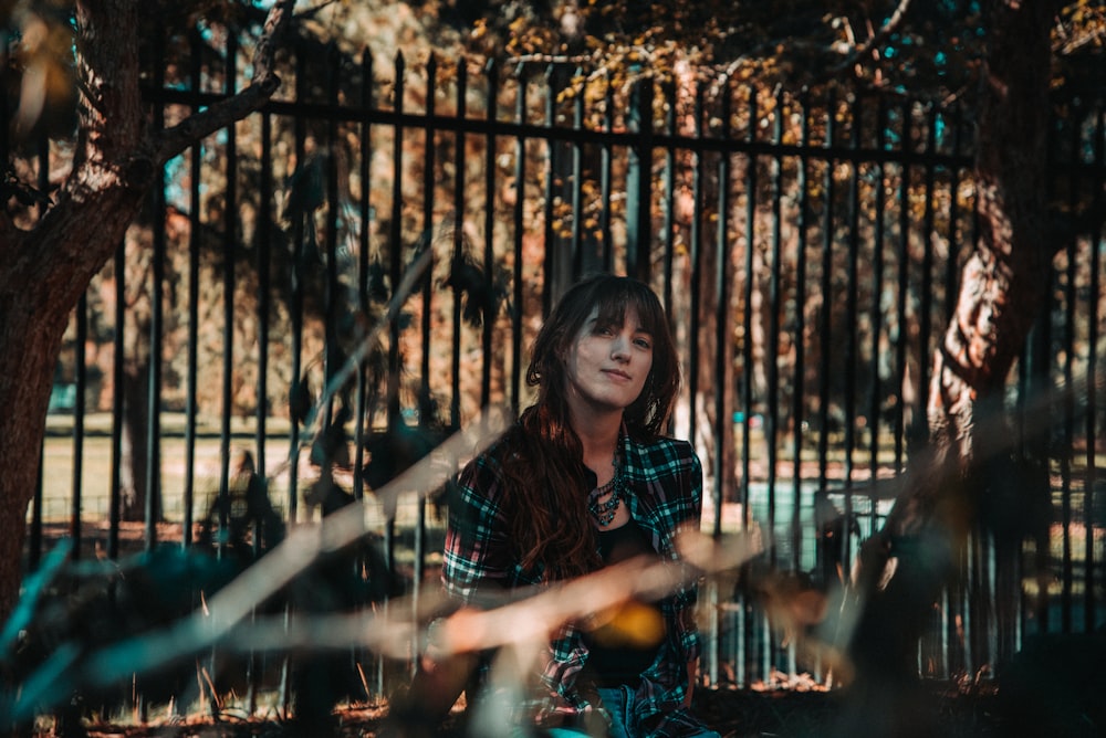 woman in black and red plaid dress shirt standing beside black metal fence during daytime