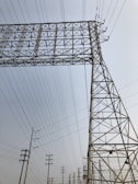 A series of tall metal power lines and pylons create a complex network against a clear sky. The structures feature intricate, geometric patterns with many intersecting lines.