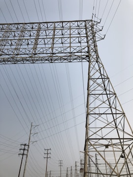 A series of tall metal power lines and pylons create a complex network against a clear sky. The structures feature intricate, geometric patterns with many intersecting lines.