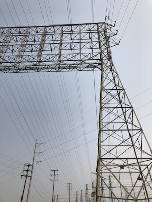 A series of tall metal power lines and pylons create a complex network against a clear sky. The structures feature intricate, geometric patterns with many intersecting lines.