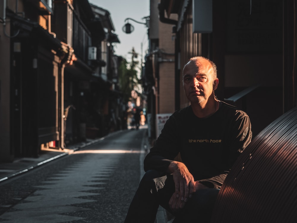 man in black hoodie sitting on sidewalk during daytime