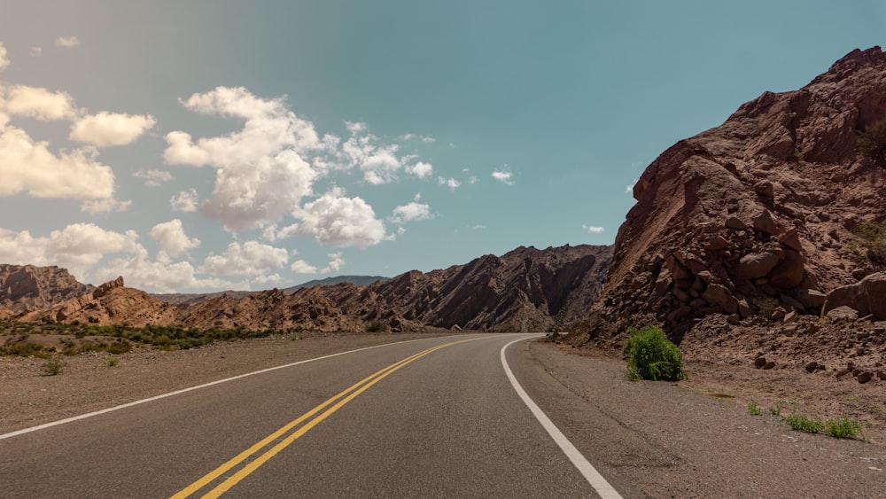 gray concrete road near brown rocky mountain under blue sky during daytime