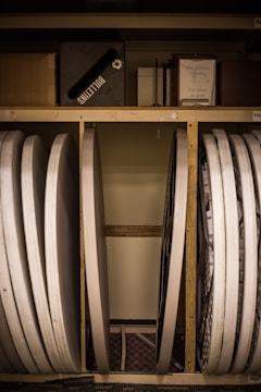 Several folded tables and a bulletin board are stored vertically against a wall. There are also various boxes and a framed paper label titled 'Blue Ribbon Offering' on the shelf above.