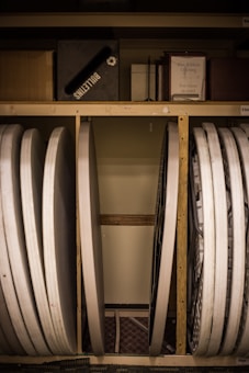 Several folded tables and a bulletin board are stored vertically against a wall. There are also various boxes and a framed paper label titled 'Blue Ribbon Offering' on the shelf above.