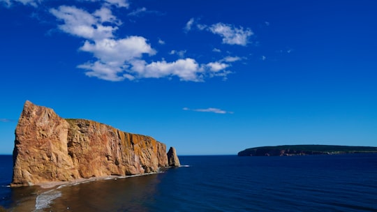 brown and green rock formation beside blue sea under blue sky during daytime in Percé Rock Canada
