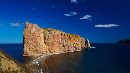 brown rock formation beside sea under blue sky during daytime in Percé Rock Canada
