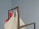 A large beige fabric bag and a smaller red bag are hanging on a black metal frame against a plain, muted blue background.