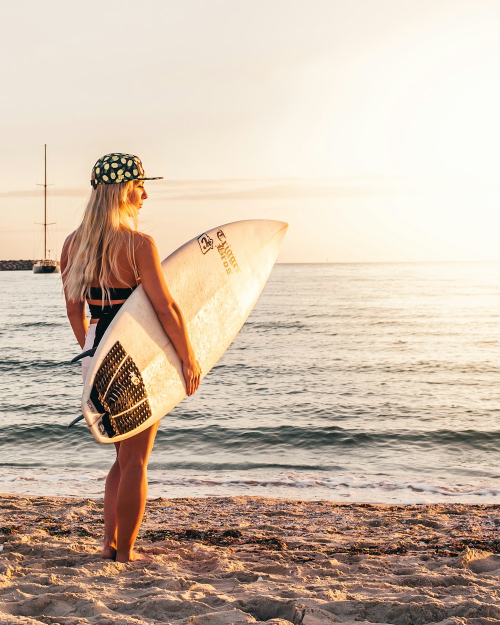 Frau im schwarzen Bikini mit Surfbrett, die tagsüber am Strand steht