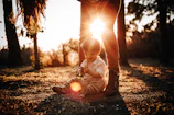 An intimate moment of a child playing with sunlight filtering through trees in a charcoal-toned setting.