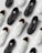 A collection of monochromatic black and white sneakers are arranged in an alternating pattern on a light gray background. The shoes have a simple design with a focus on the lace and perforation details. The black sneakers have a solid, sleek appearance while the white sneakers contrast with a clean, minimalistic look.