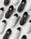 A collection of monochromatic black and white sneakers are arranged in an alternating pattern on a light gray background. The shoes have a simple design with a focus on the lace and perforation details. The black sneakers have a solid, sleek appearance while the white sneakers contrast with a clean, minimalistic look.