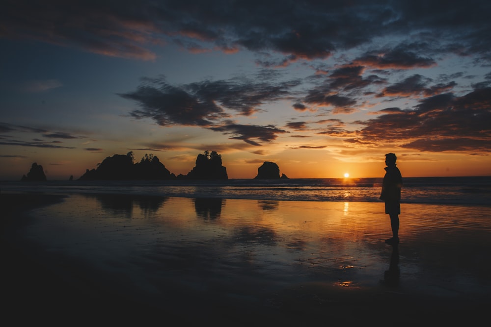 silhouette of man standing on water during sunset