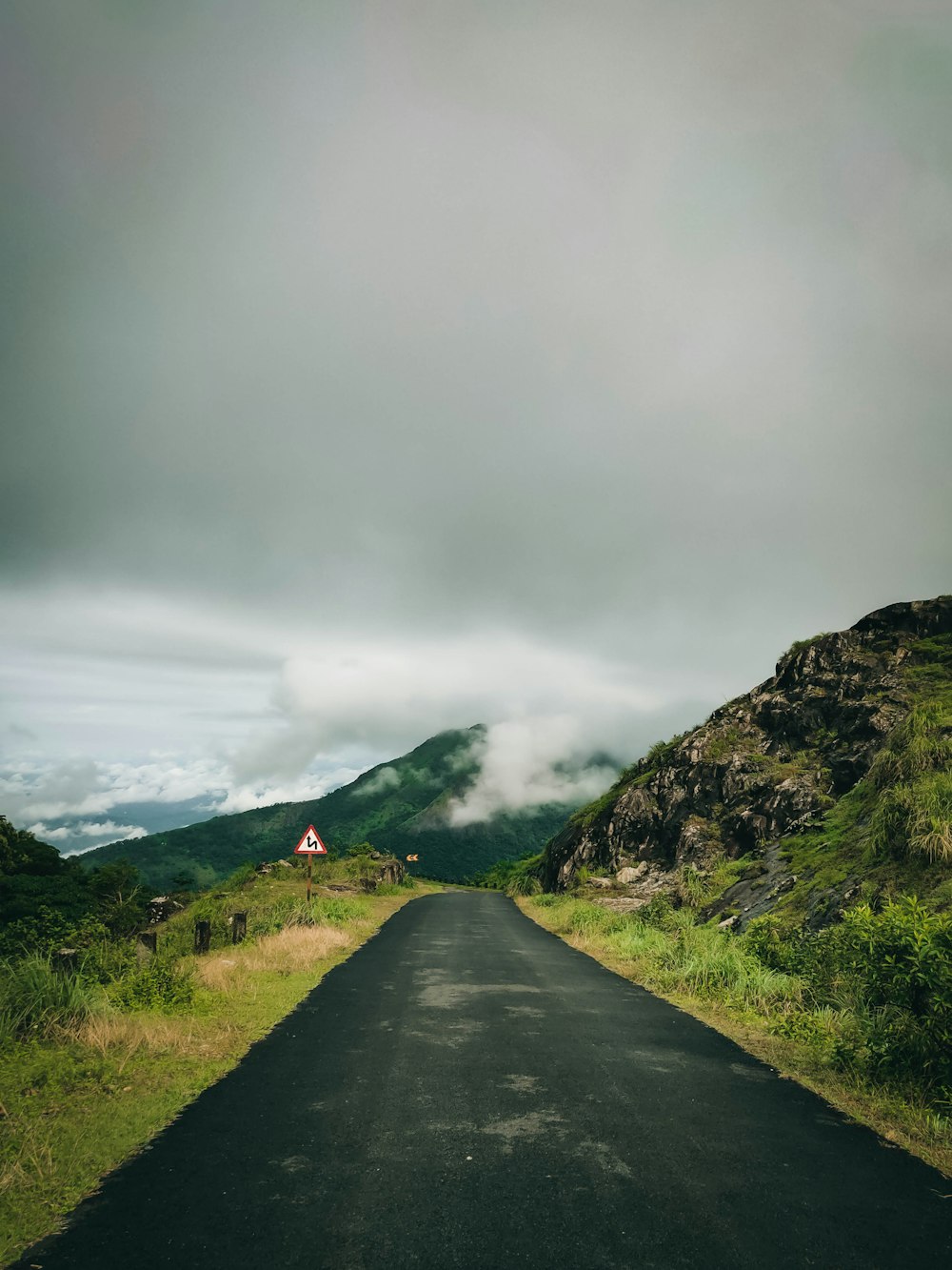 estrada de concreto cinza entre campo de grama verde perto da montanha sob nuvens cinzentas durante o dia