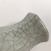 A close-up of a ceramic object featuring a distinctive craquelure pattern, with a glossy surface reflecting light. The object has a curved shape and appears to be a part of a vase or a ceramic piece.
