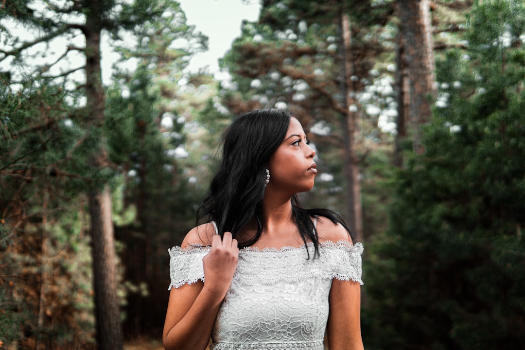 woman in white lace floral dress standing near green trees during daytime