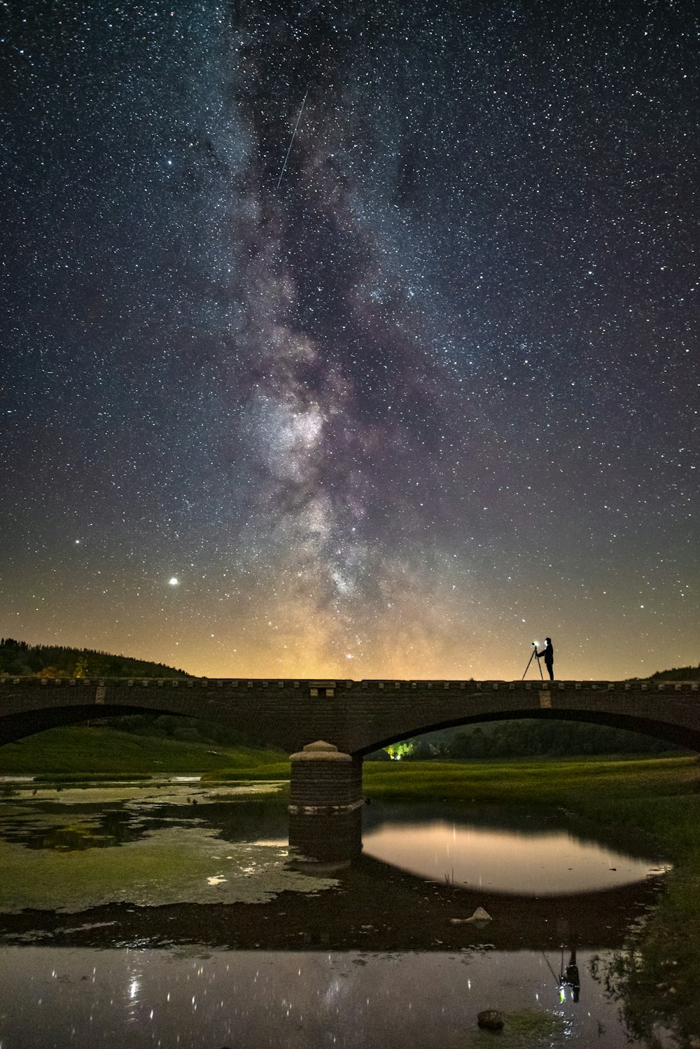 man standing on bridge under starry night