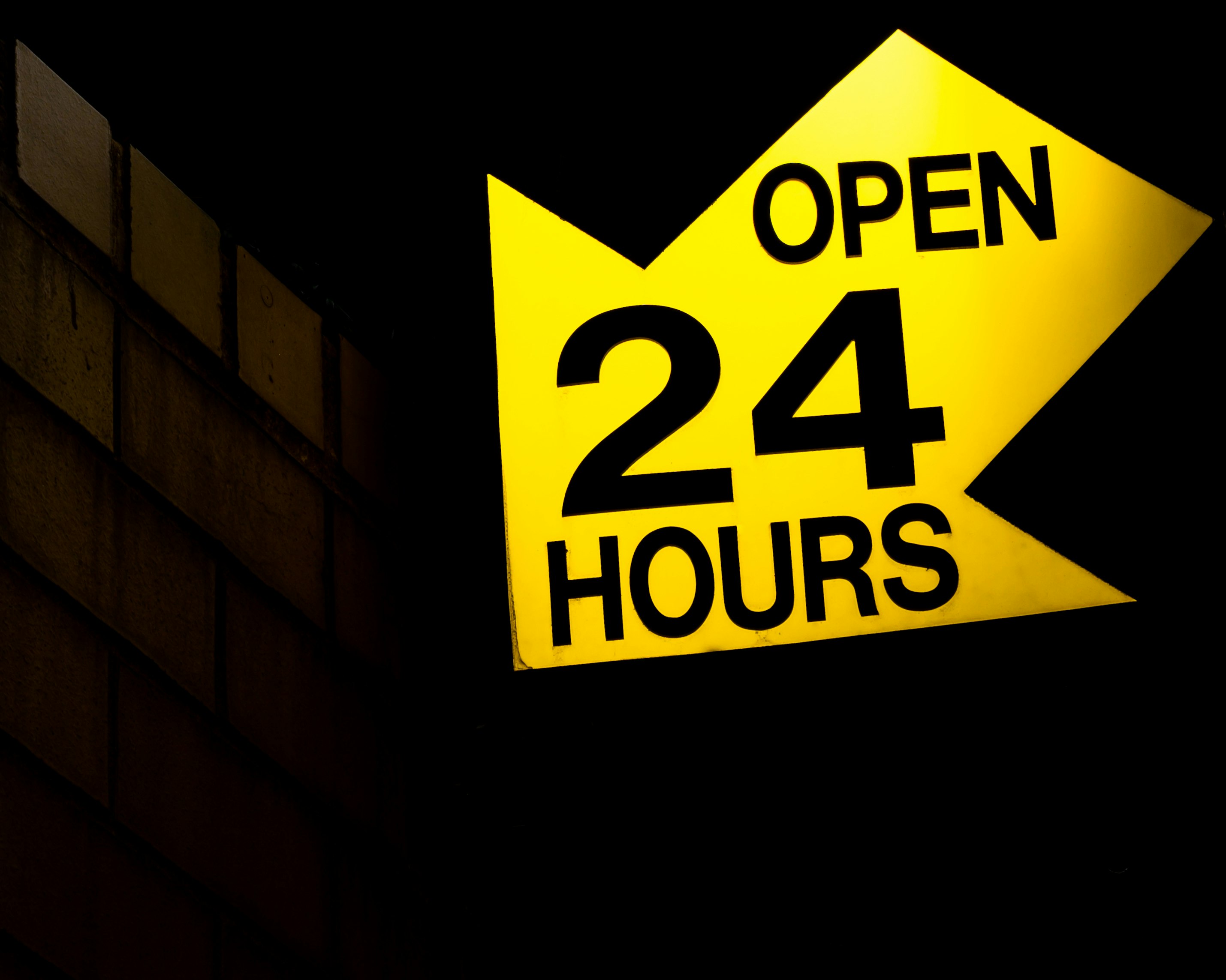 Yellow arrow shaped sign that reads open 24 hours. 
