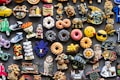A colorful assortment of decorative fridge magnets depicting various objects such as donuts, animals, owls, fruits, and Italian-themed items. The magnets are arranged closely together on a dark background, showcasing a wide variety of shapes and designs, including smiley faces and motorcycles.