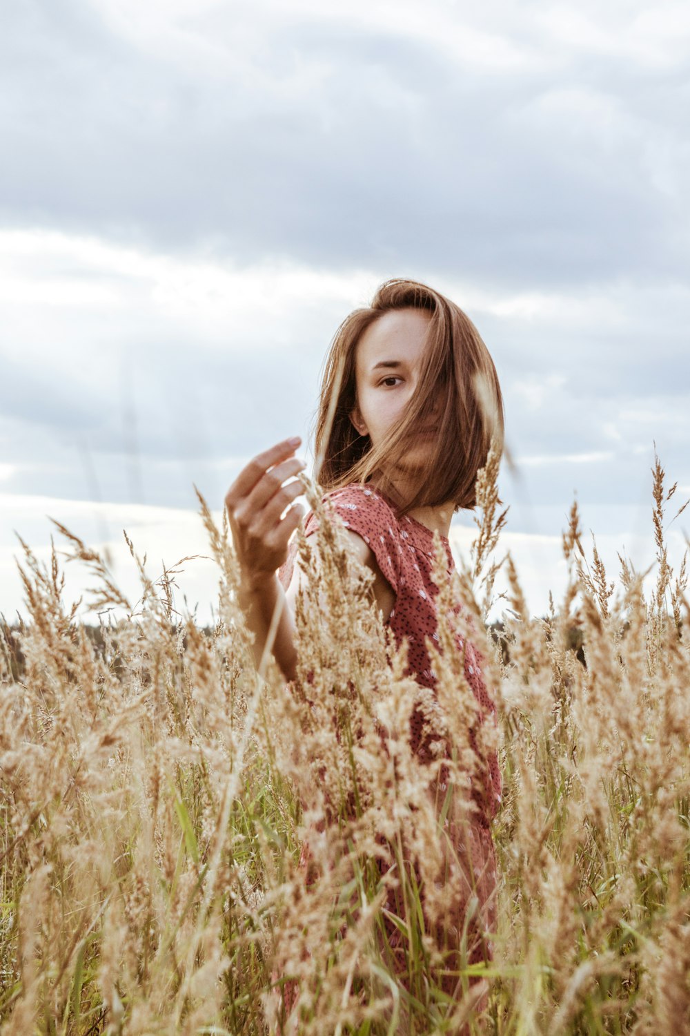 woman in brown and white floral dress standing on wheat field during daytime