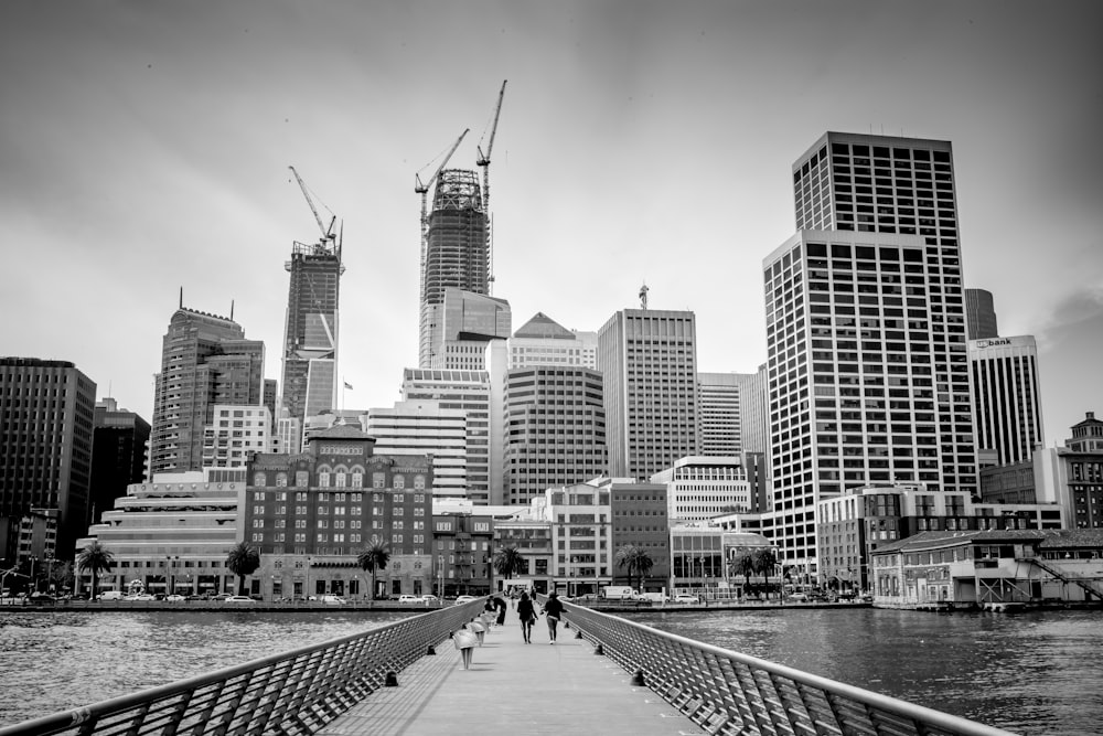 grayscale photo of people walking on sidewalk near city buildings