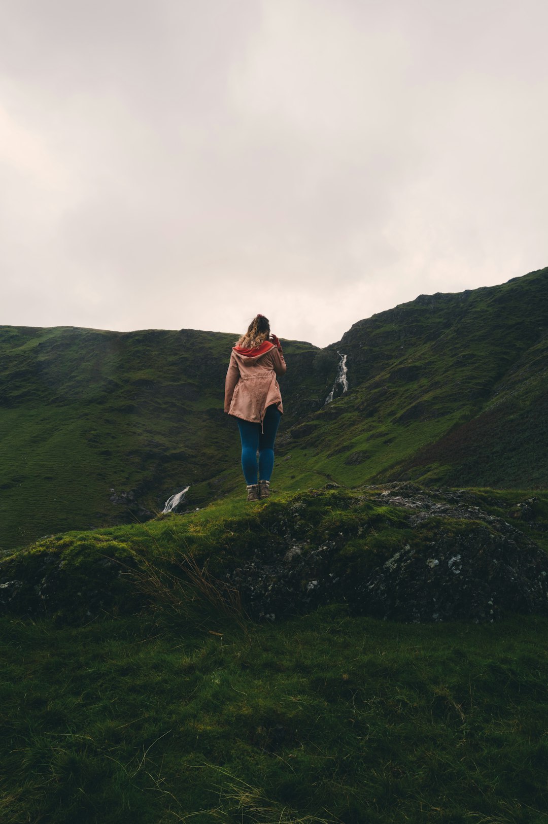 woman in brown jacket and blue denim jeans standing on green grass field during daytime