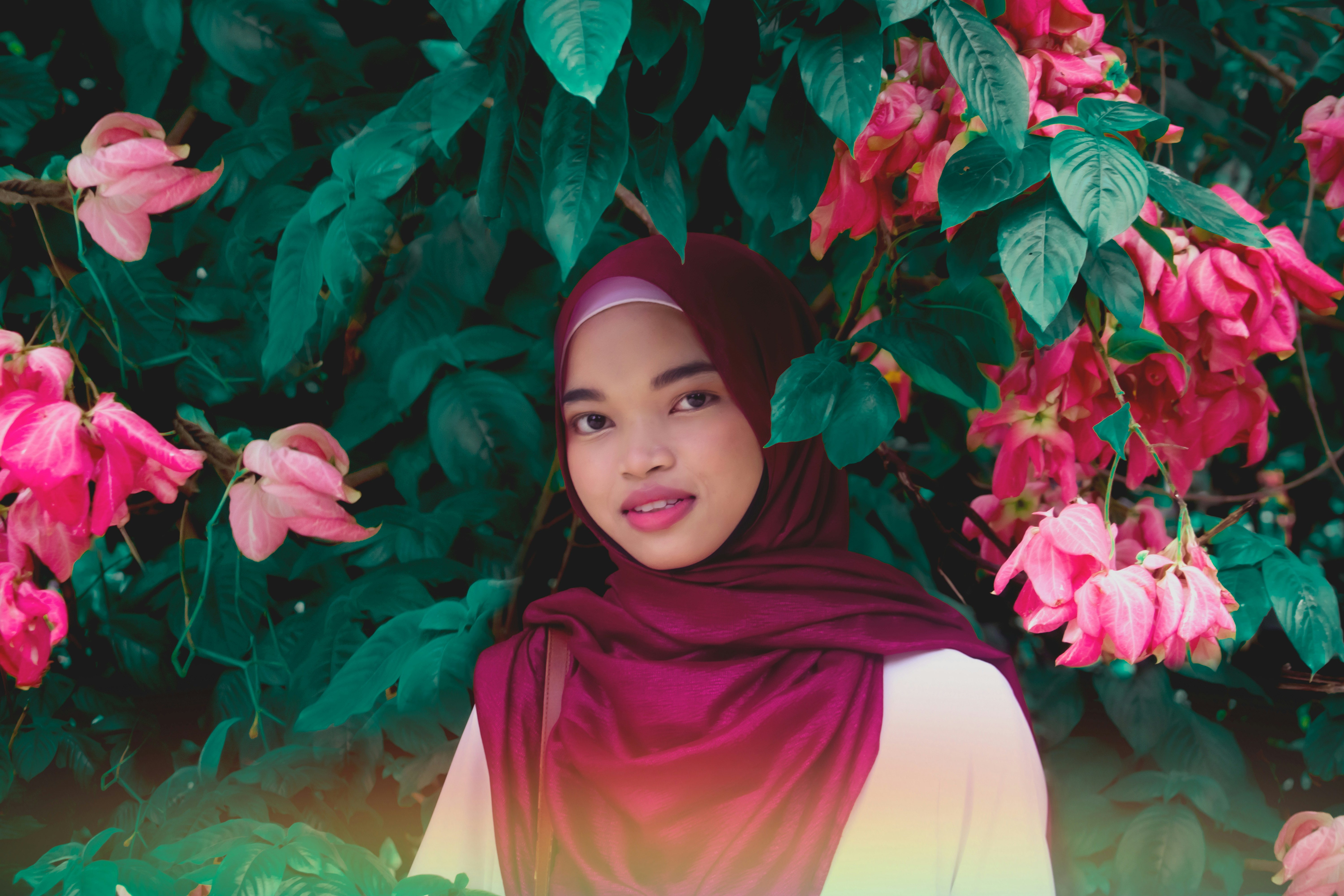 woman in red hijab standing beside red flowers